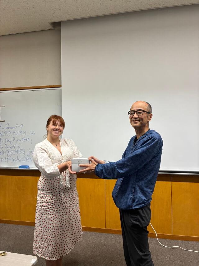 誕生日ケーキの箱を手渡す外国人の学生と、そのケーキを受け取るにこやかな松岡さん。